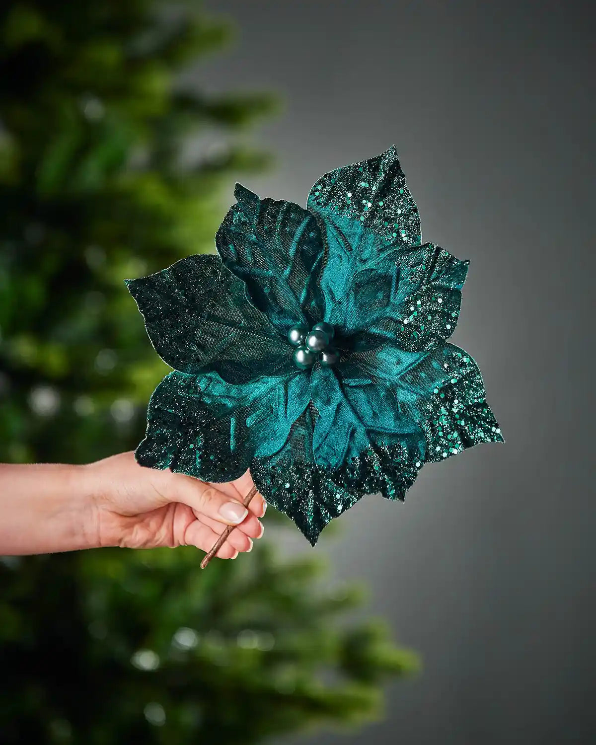Emerald glittery flower held by a hand against a grey background