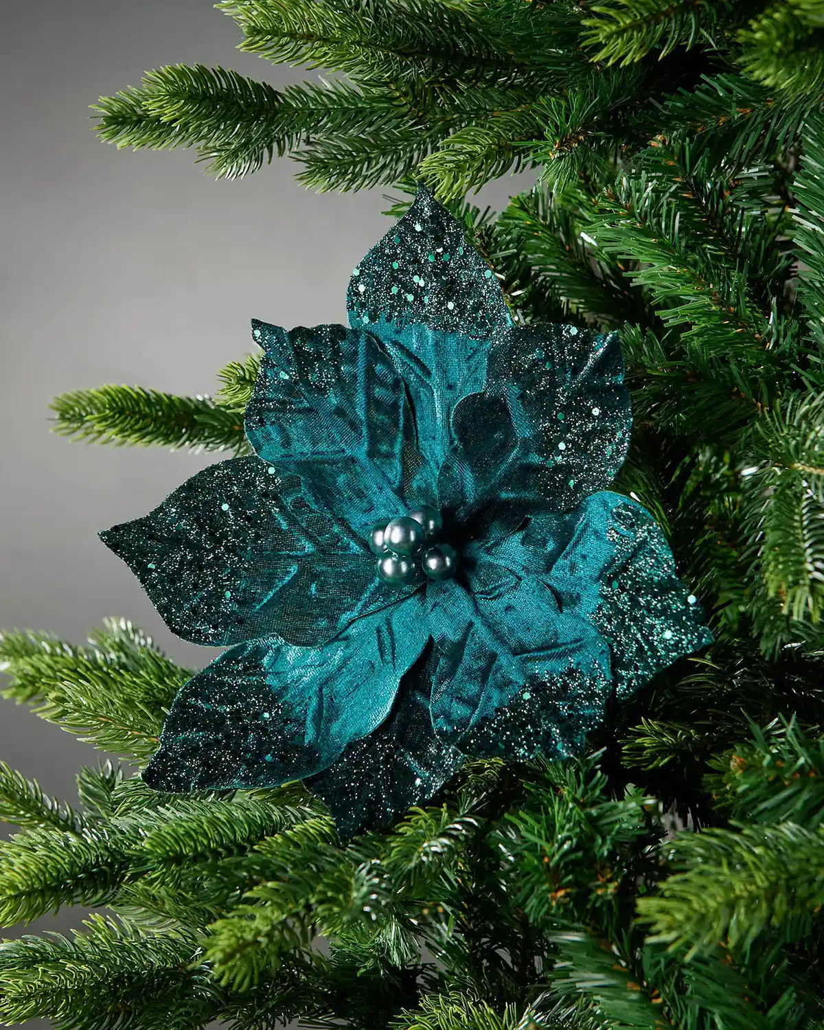 Emerald glittery flower ornament on a Christmas tree branch