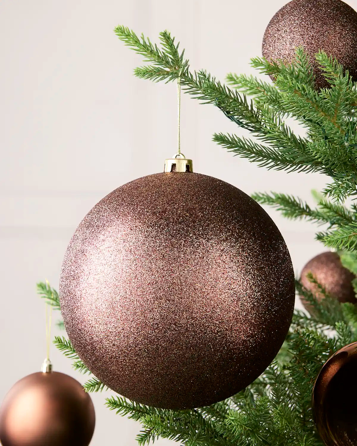 Espresso 20 cm oversized Glitter shatterproof bauble displayed on a Christmas tree with coordinating Espresso baubles.
