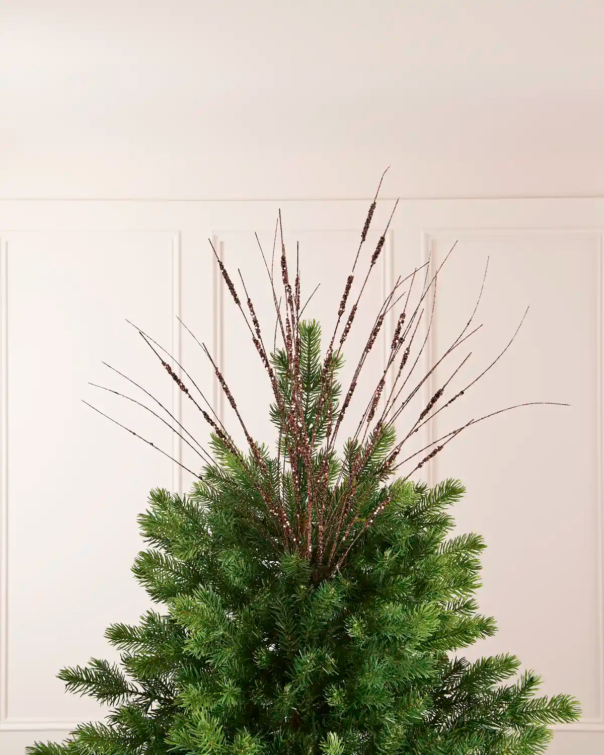 Espresso Glitter Wispy Spray displayed at the top of a Christmas tree, with thin glitter-covered stems extending upward and outward
