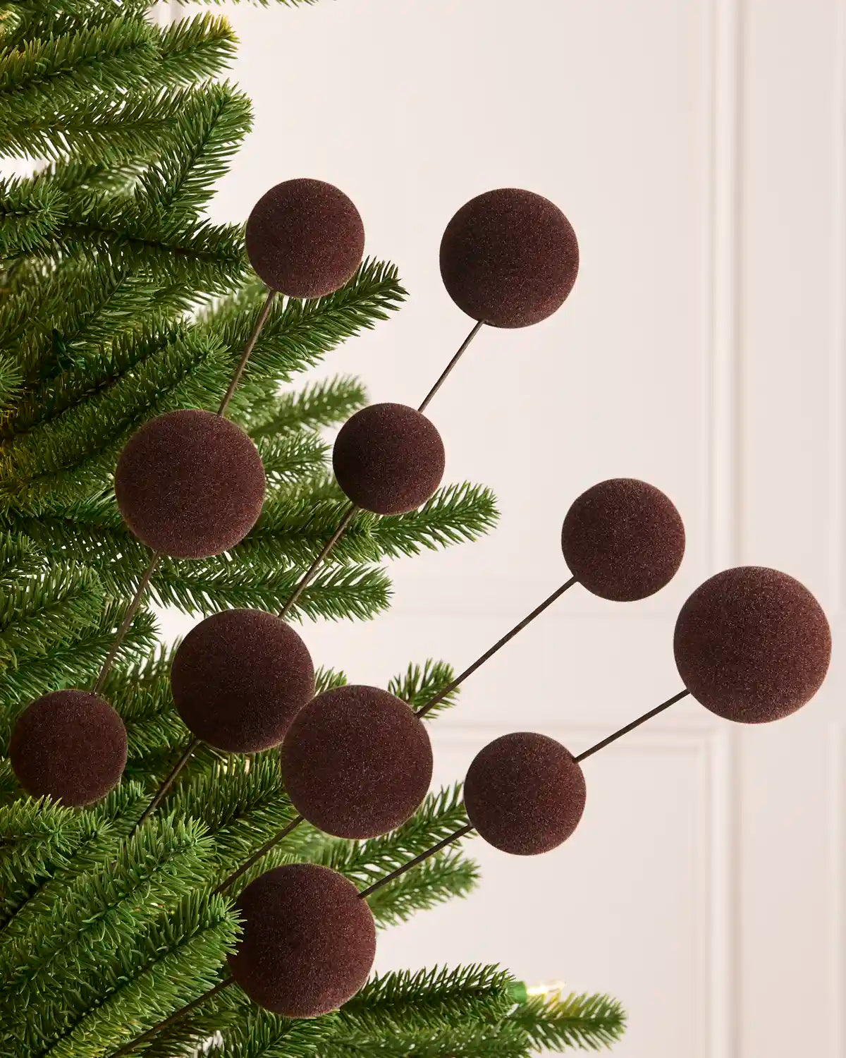 Espresso Velvet bauble tree pick on thin black stems, shown hanging on green artificial pine branches against a light cream background. 