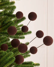 Espresso Velvet bauble tree pick on thin black stems, shown hanging on green artificial pine branches against a light cream background. 