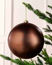 Espresso coloured oversized bauble hanging on a Christmas tree with gold string against a cream background 