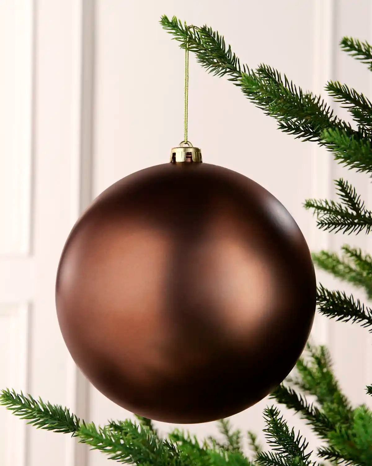Espresso coloured oversized bauble hanging on a Christmas tree with gold string against a cream background 