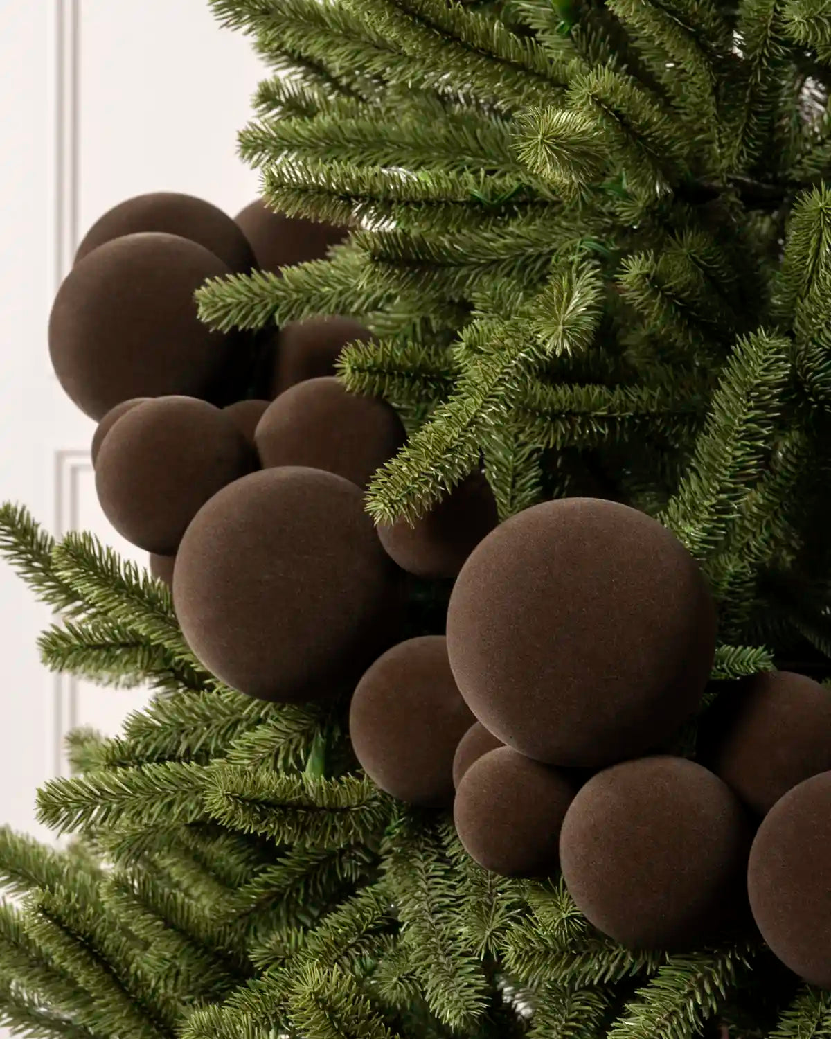 Espresso coloured velvet Christmas tree ornaments clustered on green artificial pine branches.