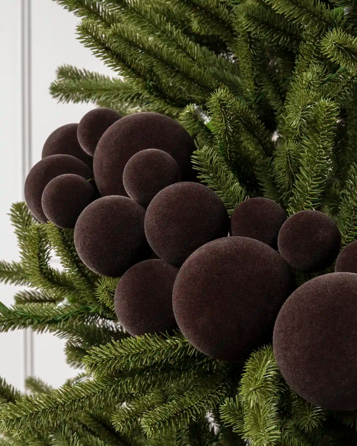 Espresso coloured velvet Christmas tree ornaments shaped like clusters of pinecones, nestled among green artificial pine branches.