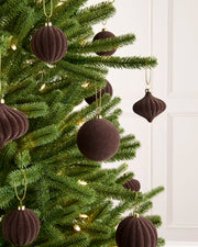 Espresso coloured velvet baubles shaped in various shapes, ribbed and smooth finishes hanging on gold string on a Christmas tree against a light background