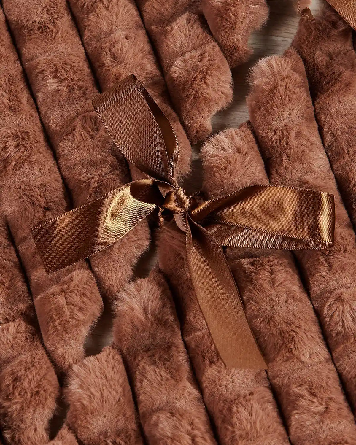 Close-up of the espresso faux fur diamond tree skirt ribbon ties on light wooden flooring