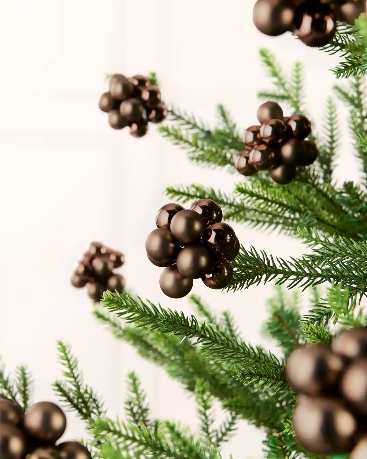 Espresso glass berry cluster baubles arranged throughout a green Christmas tree.

