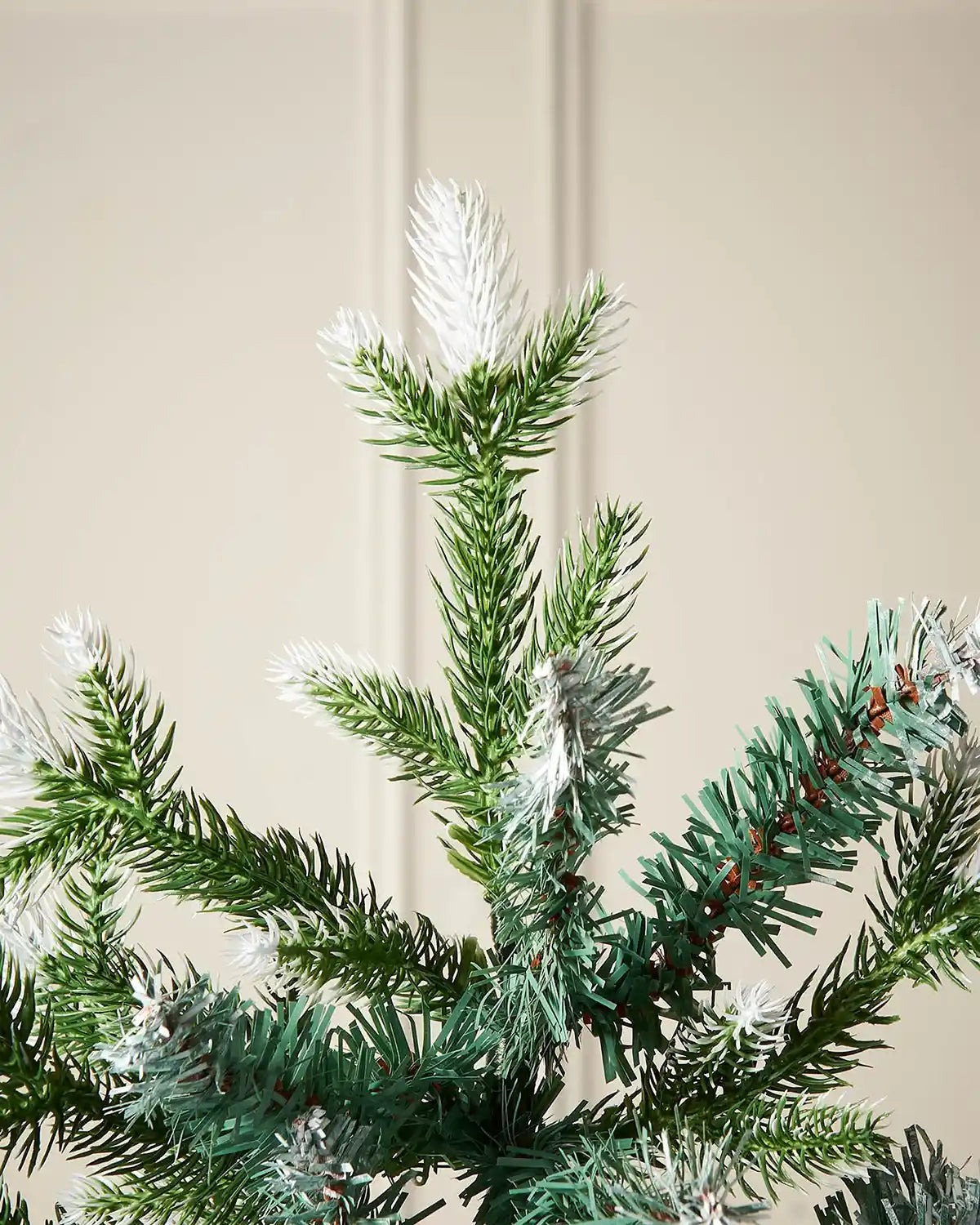 Close up of the top pf the tree showing PVC and PE snow flocked tips at the on the Evergreen Snow Flocked Tip Christmas Tree, 6 ft on a panel textured background
