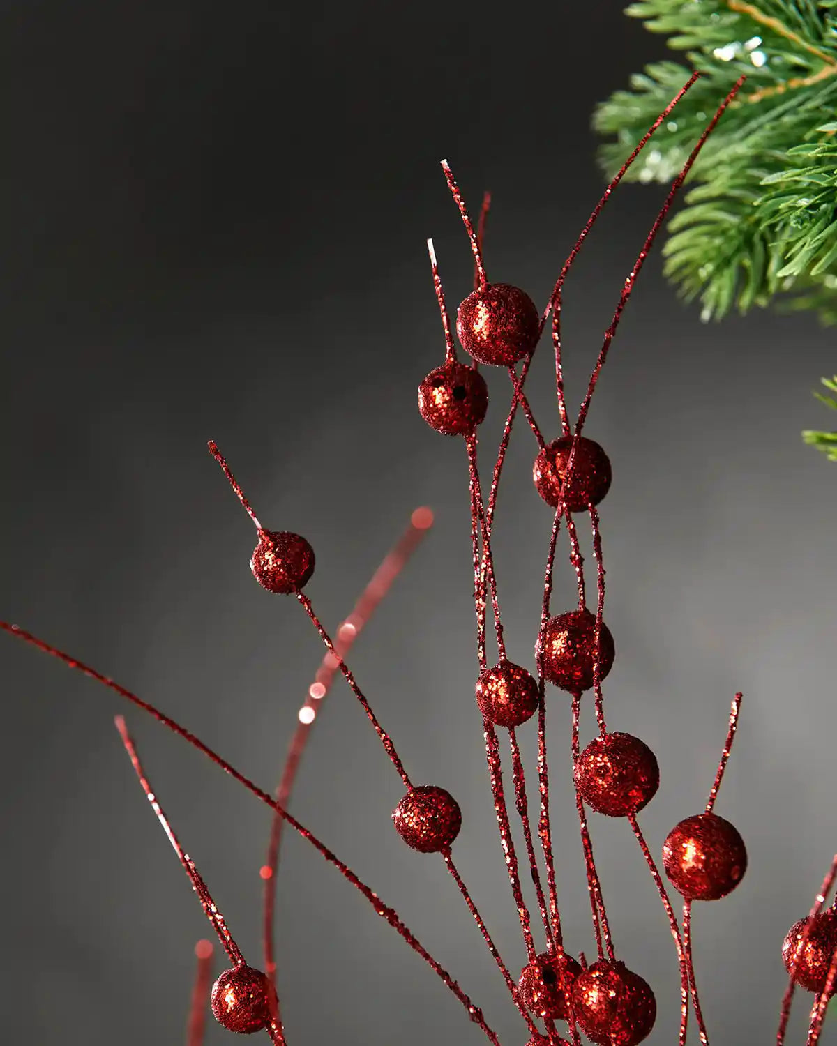 Extra close-up red glitter berries spray in front of grey wall background highlighting glitter effect