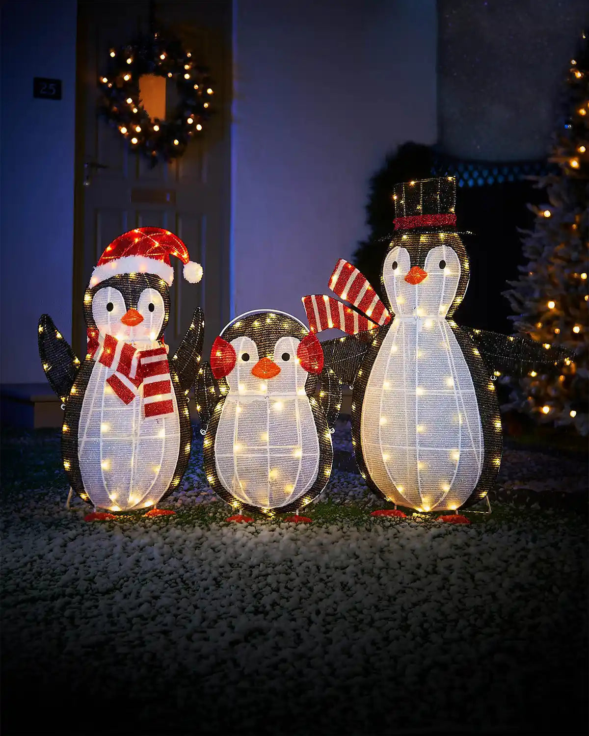 Family of LED penguins on snowy grass in the garden in front of a decorated Christmas tree