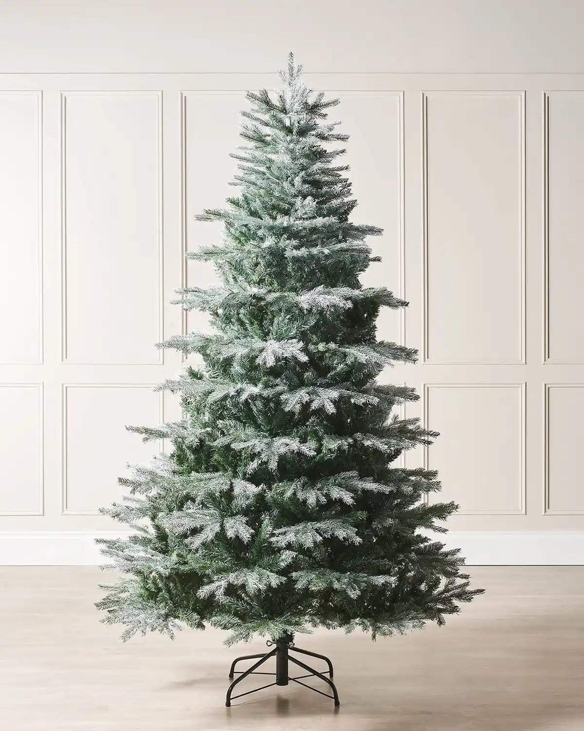 Festive frosted Christmas tree against a neutral wall.