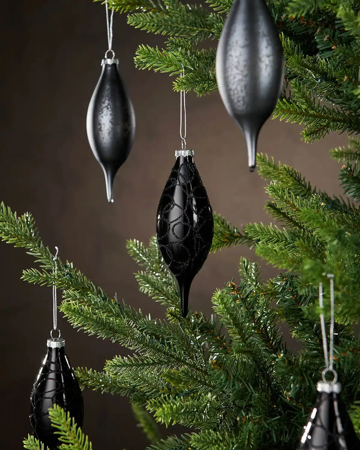 Five Black decorative baubles hanging on a Christmas tree with a brown background