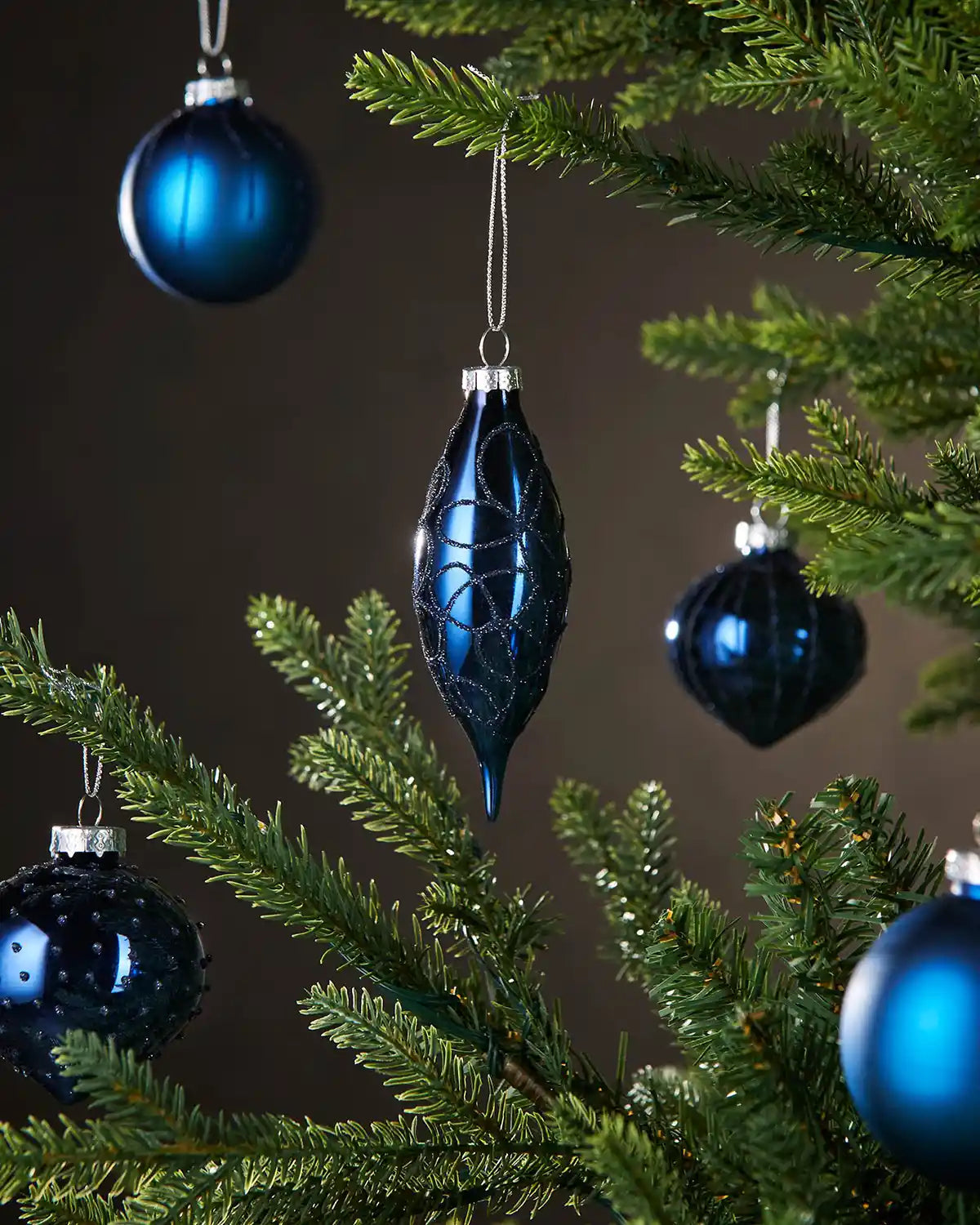 Five Blue glass baubles on a Christmas tree against a dark background