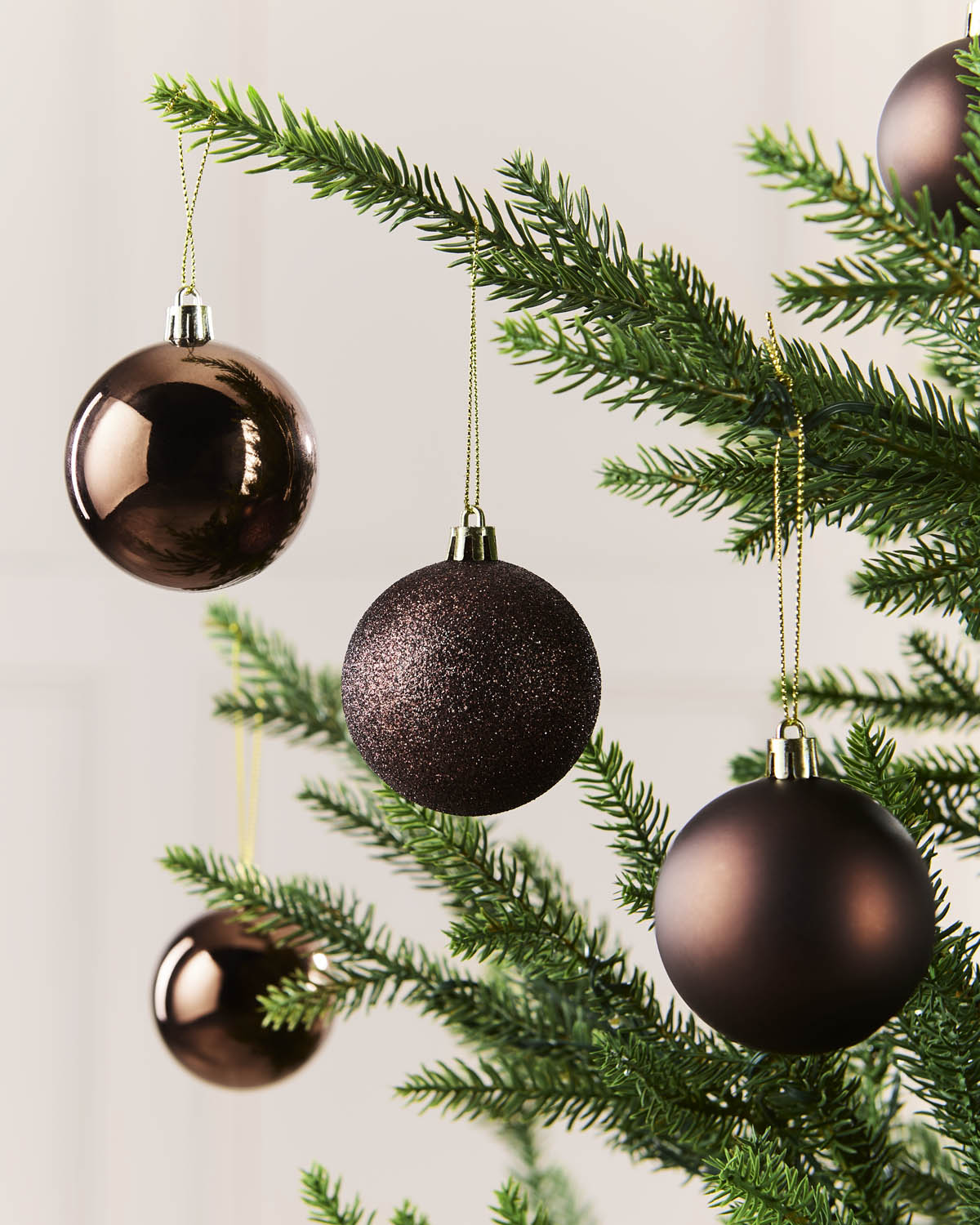 Five Espresso Christmas tree ornaments in different textures and finishes hanging from the green branches of a Christmas tree against a light background.