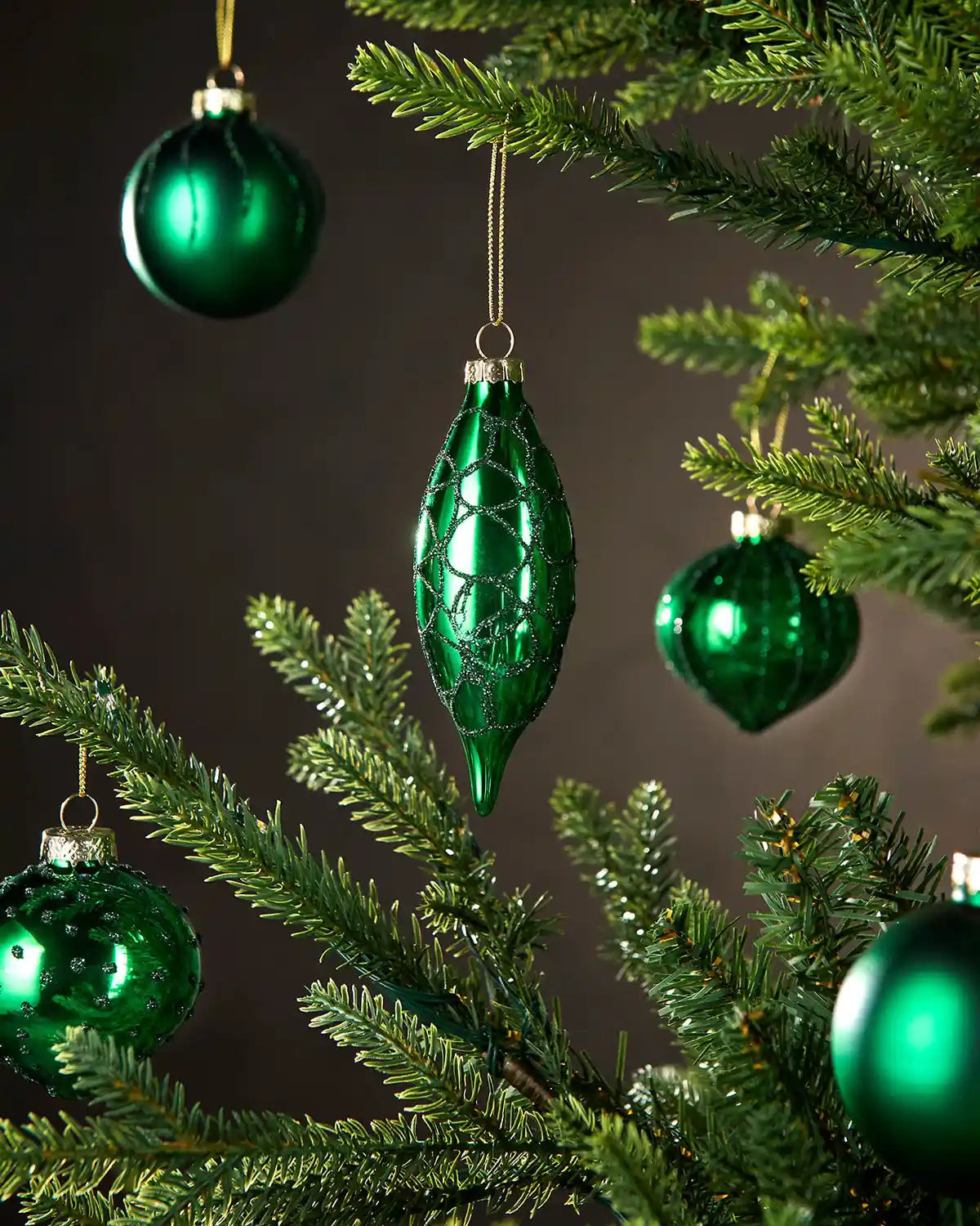 Five Green Christmas baubles on a tree against a dark background