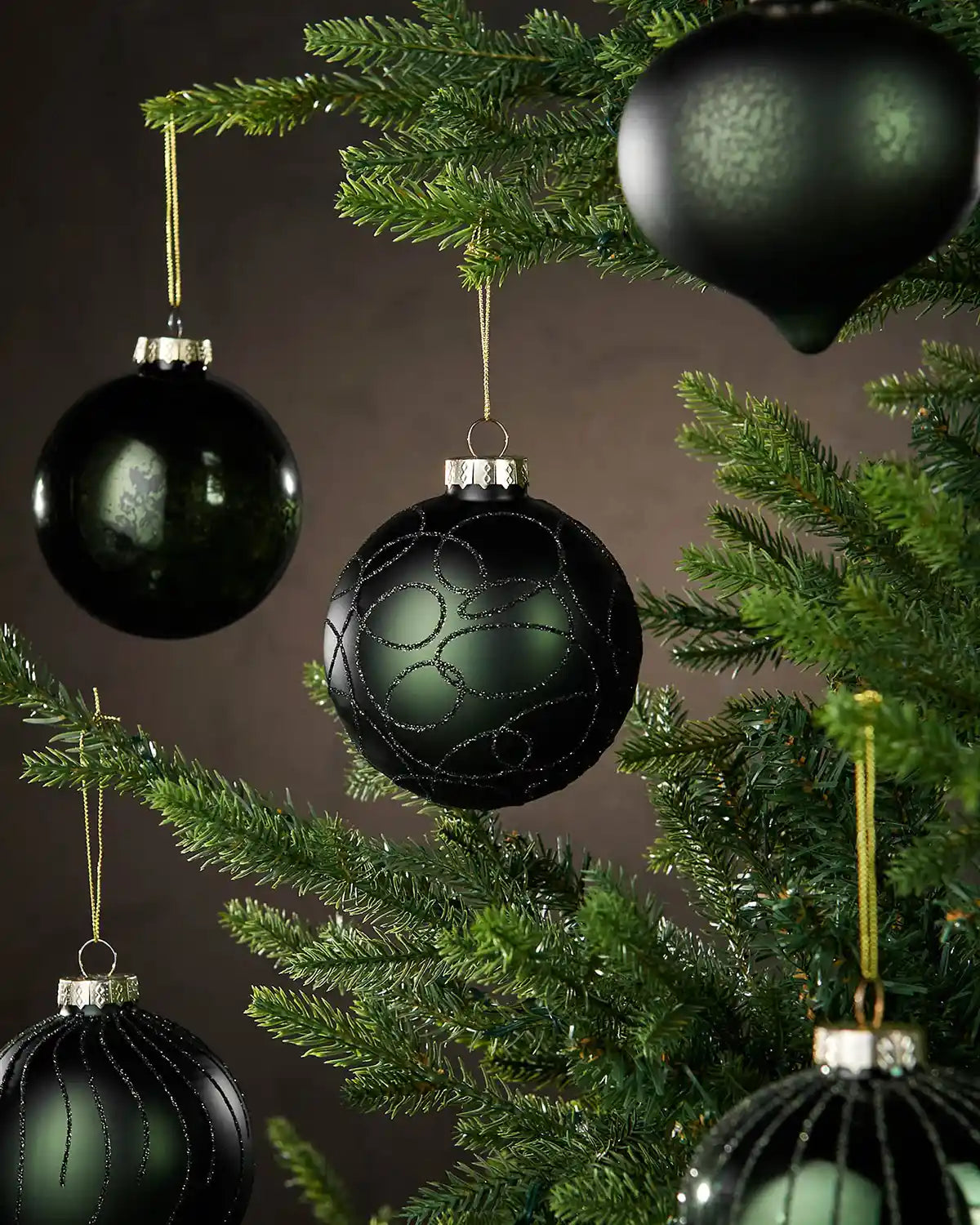 Five Sage green various shaped Christmas baubles hanging on a tree branch with a brown background