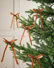 A set of five espresso velvet bows on Christmas tree branches in front of a white background