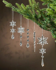 Five hanging glass crystal ornaments with snowflakes and rain drop patterns on a Christmas tree against a brown background