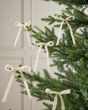 A set of five latte velvet bows on the edge of Christmas tree branches in front of a white background