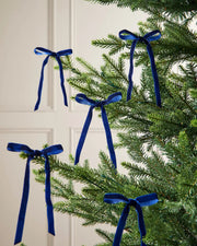 A set of five navy blue velvet bows on the edge of Christmas tree branches in front of a white background