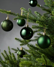Five sage green baubles hanging on a Christmas tree with a grey blurry background