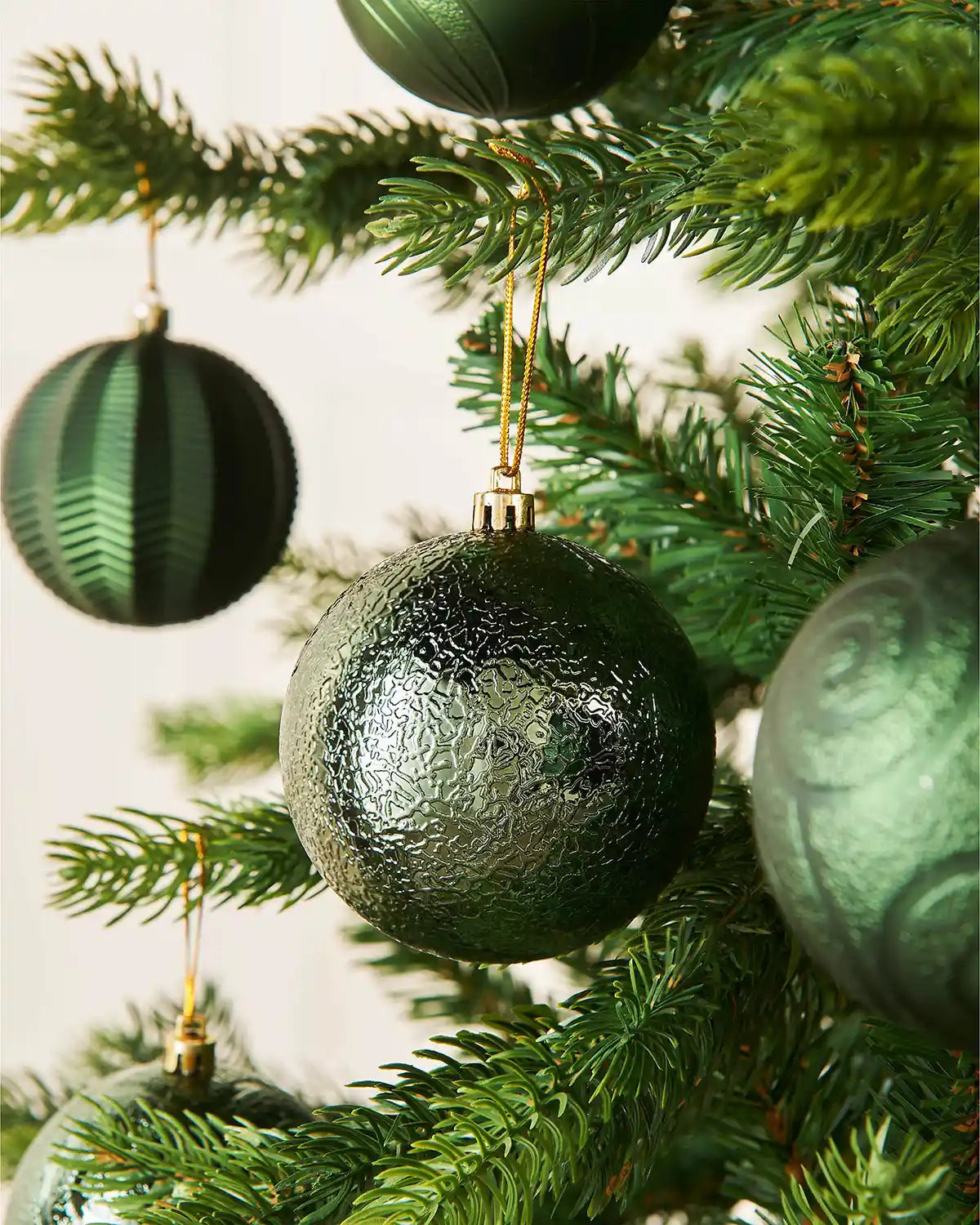 Five sage green baubles on a Christmas tree with a blurry cream background 