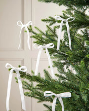 A set of five white velvet bows on the edge of Christmas tree branches in front of a white background