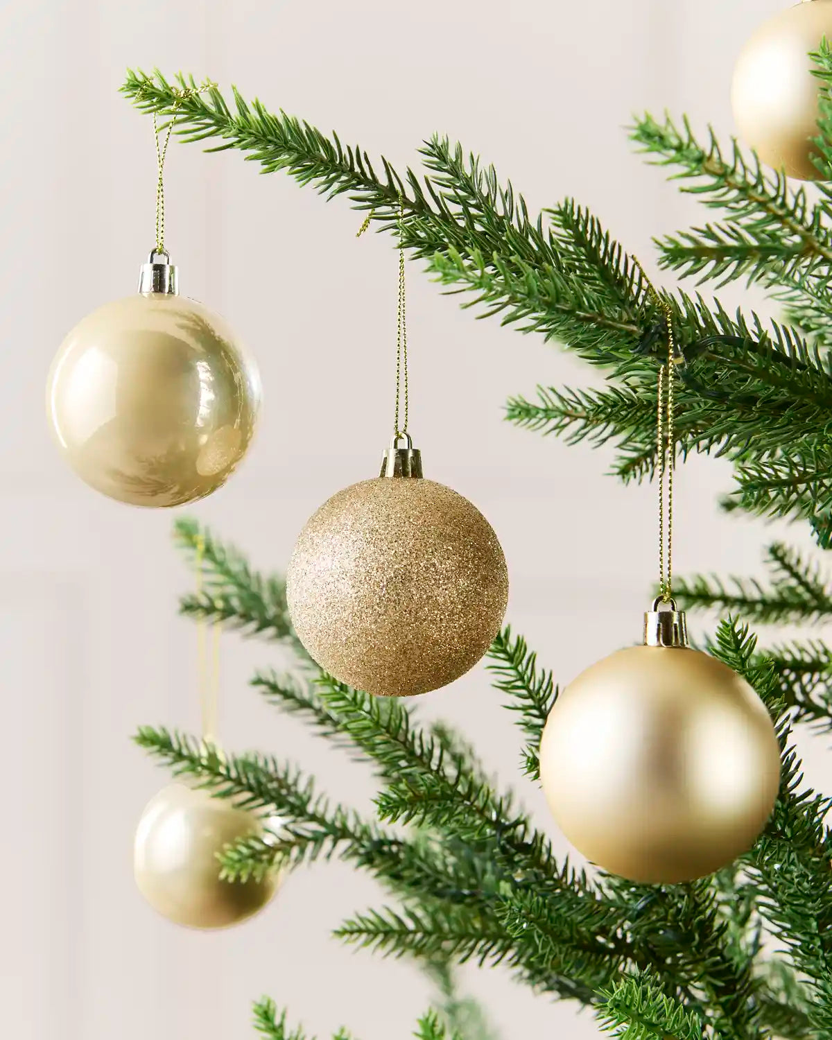 Four Latte coloured Christmas tree ornaments hanging from green pine branches against a soft light background.
