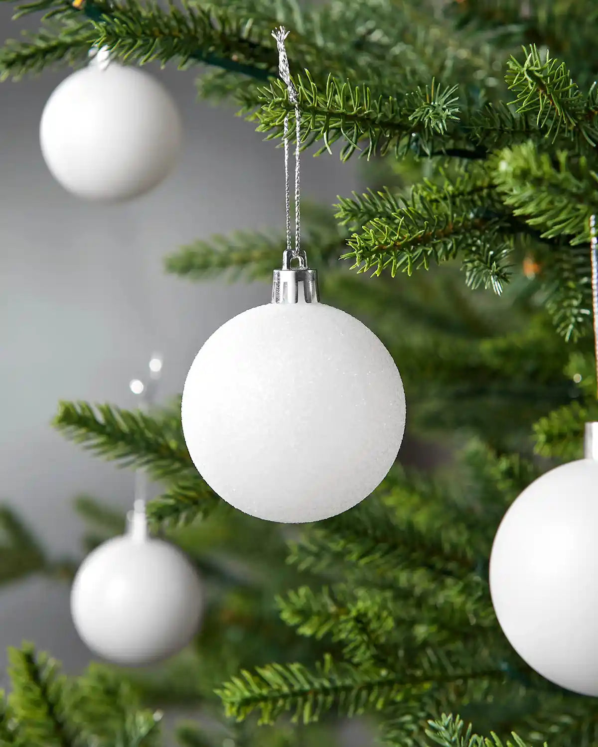 Four White baubles hanging on a Christmas tree against a blurry grey background