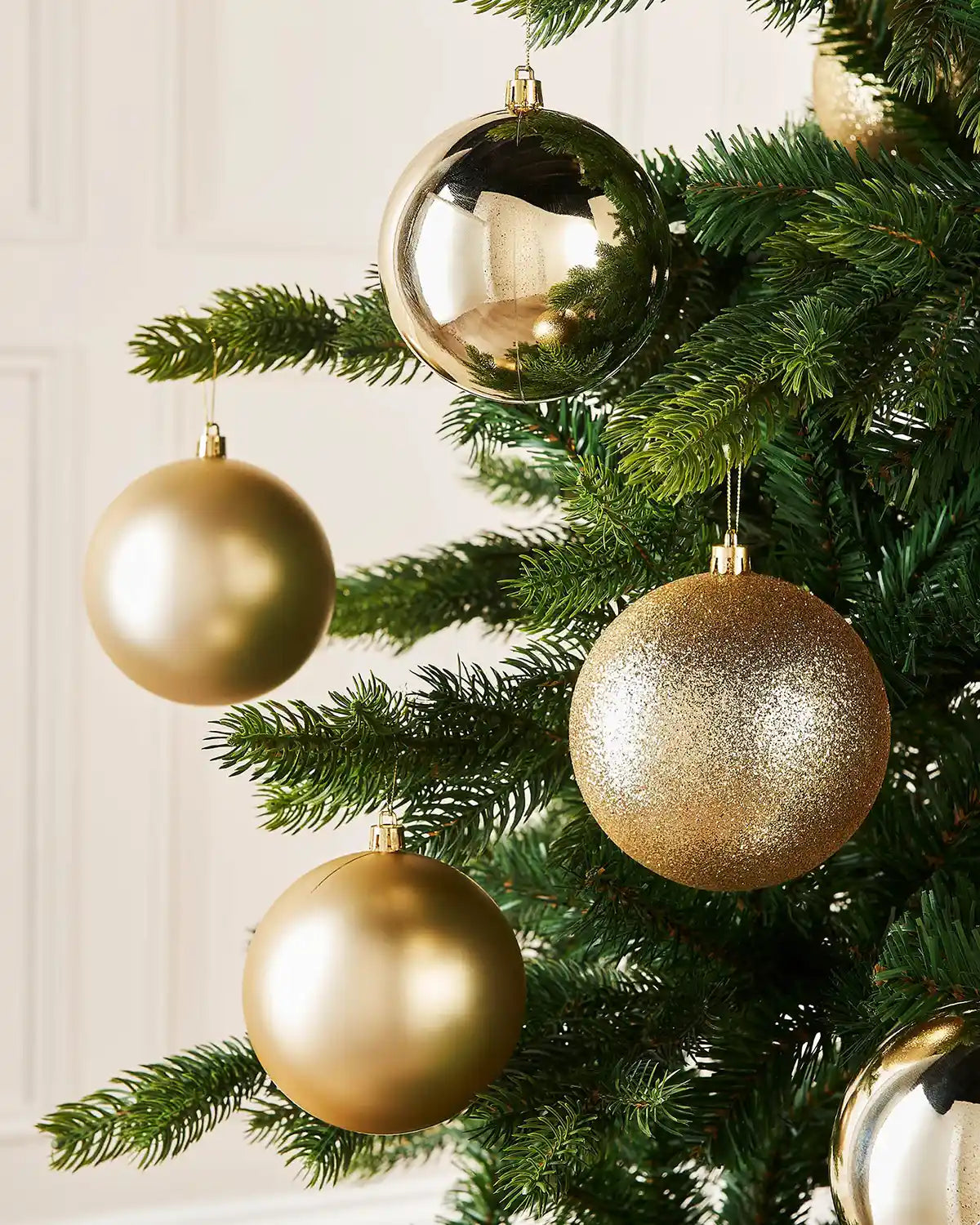 Four gold baubles on a Christmas tree branch against a cream panel wall