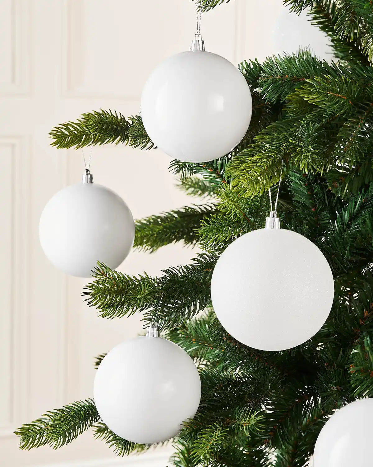 Four white baubles on a Christmas tree branch against a cream background