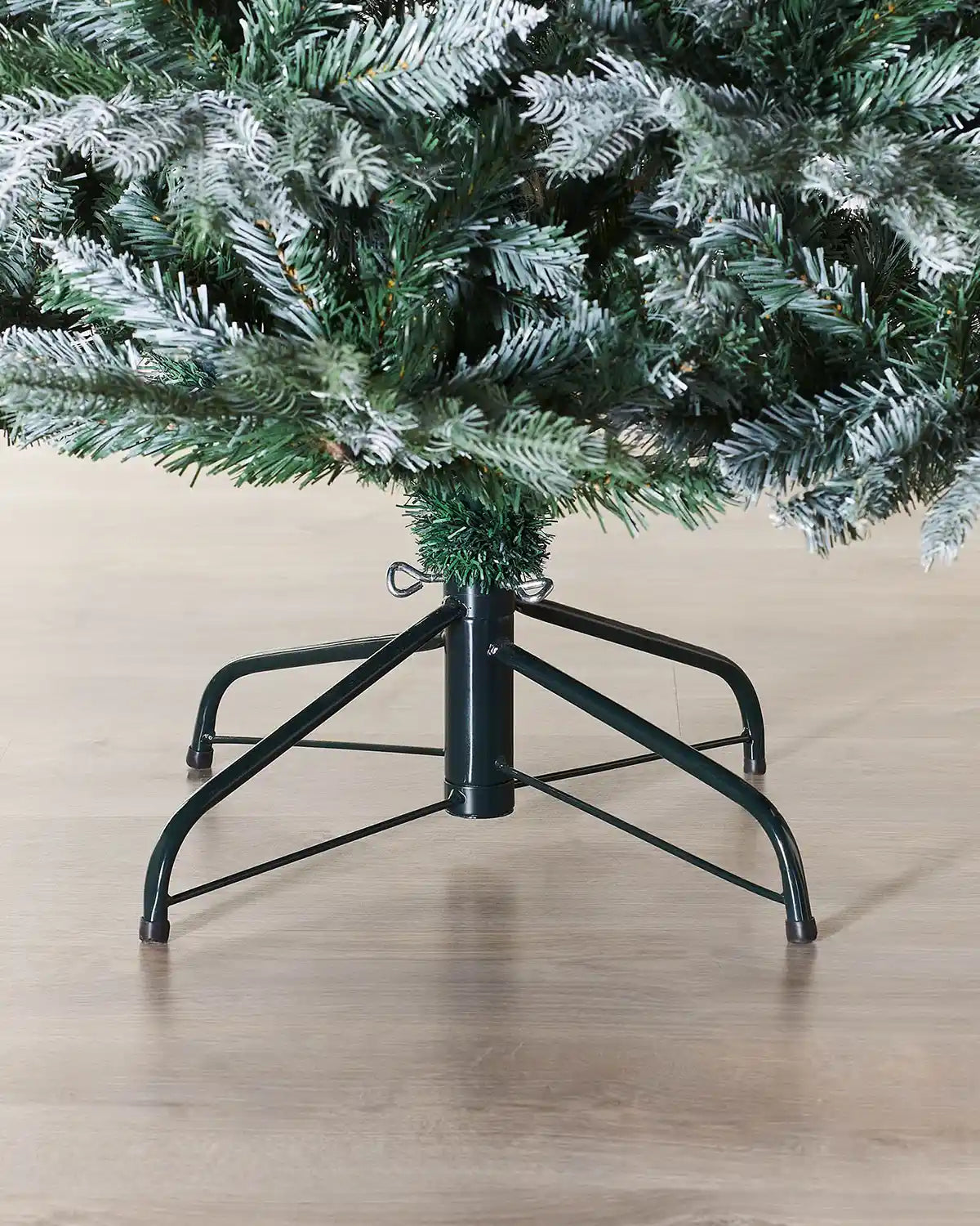 Frosted Christmas tree stand with a green artificial Christmas tree on a wooden floor