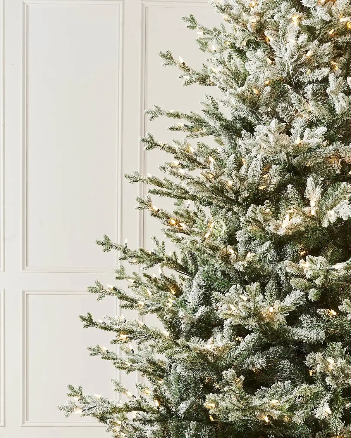 Frosted Christmas tree with warm white lights against a white panelled wall