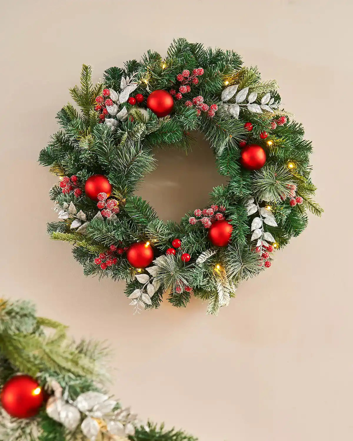 Frosted Christmas wreath with red berries and lights on a white background on a beige background