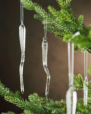 Frosted Icicle-shaped Christmas ornaments hanging on a tree branch with a blurred background