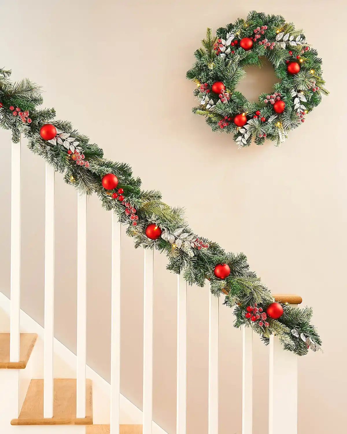 Frosted red berry garland draped on white wooden staircase with the matching frosted wreath hanging above