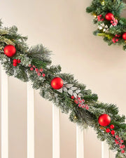 Frosted garland decorated with Red baubles, berries and frosted leaves on a staircase banister with half a matching wreath in background