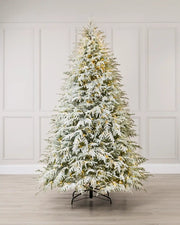 Full-length view of a flocked artificial Christmas tree illuminated with warm white lights in a minimalist, neutral interior