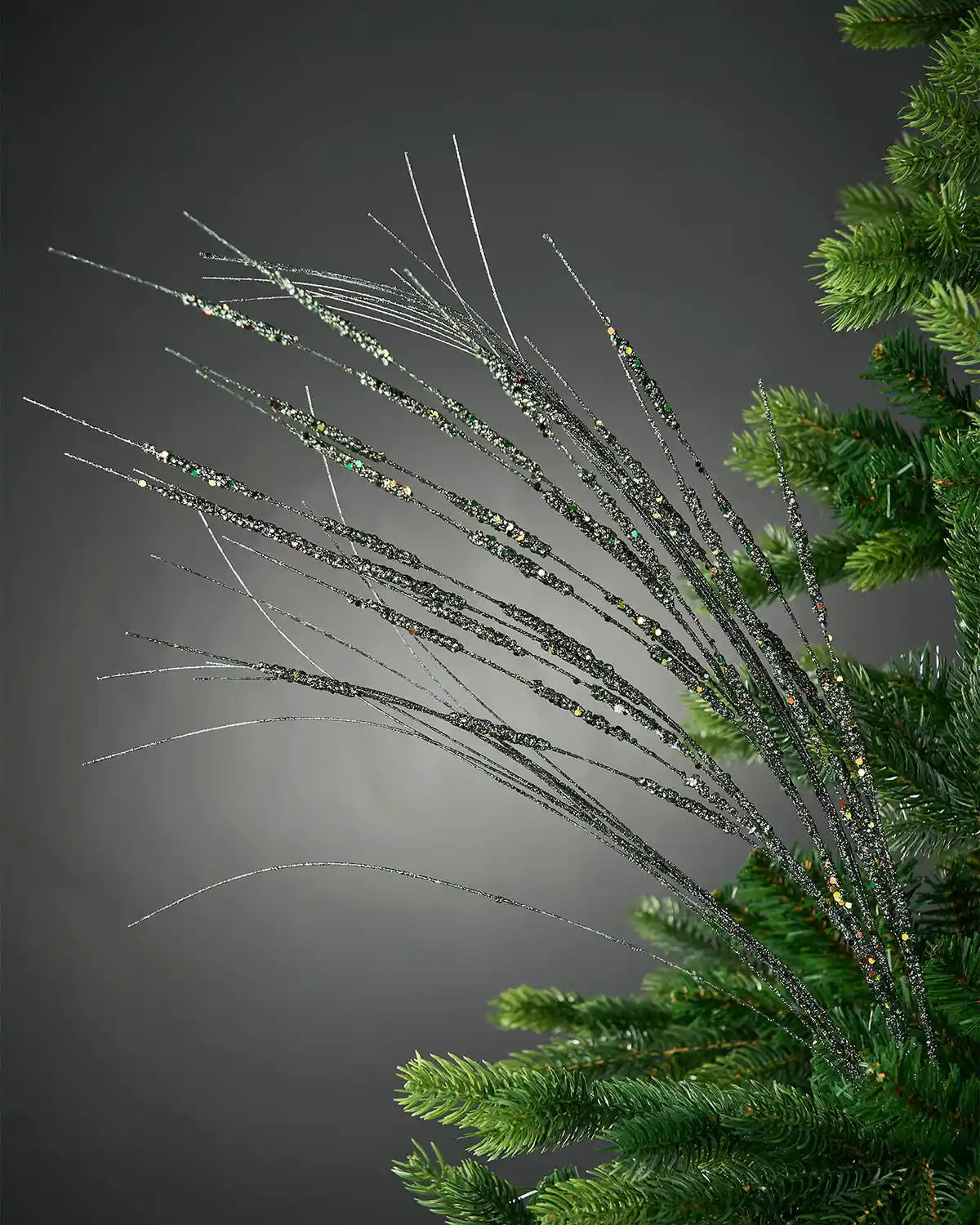 Full image of 100cm sage green glitter wispy tree spray attached to Christmas tree in front of grey wall background