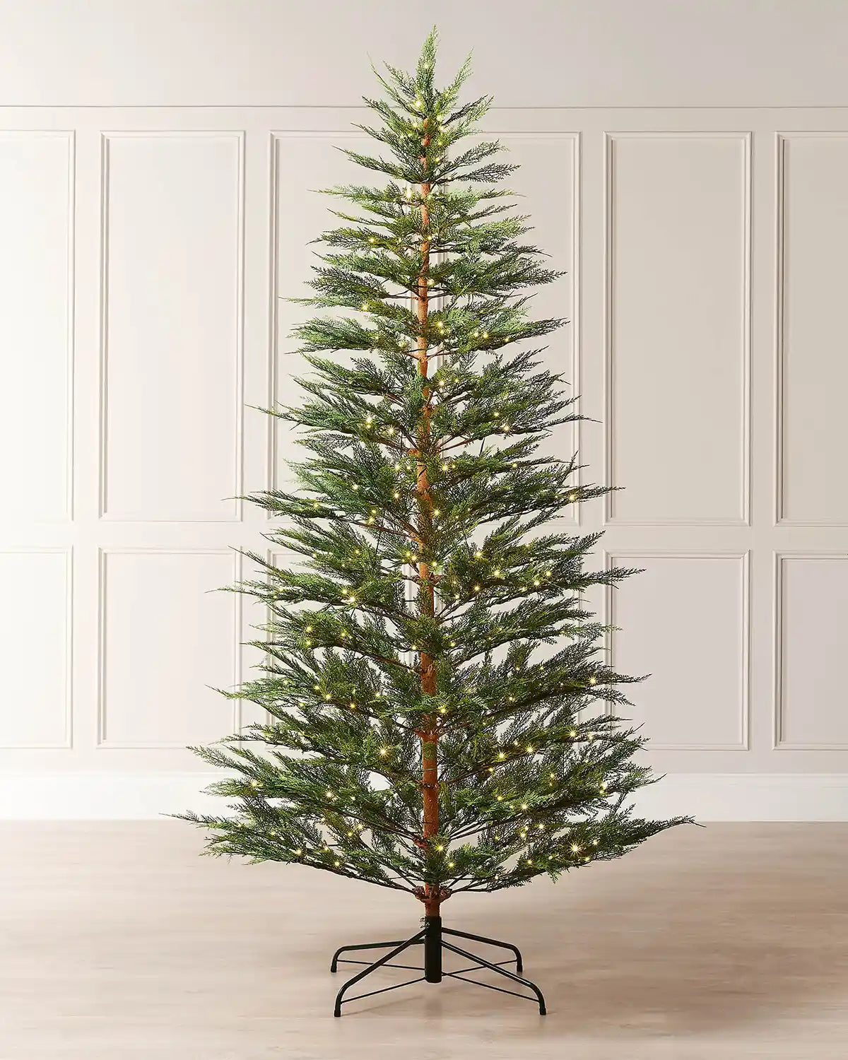 Full image of 6.5ft pre-lit cypress fir Christmas tree with warm white light setting in front of white panelling