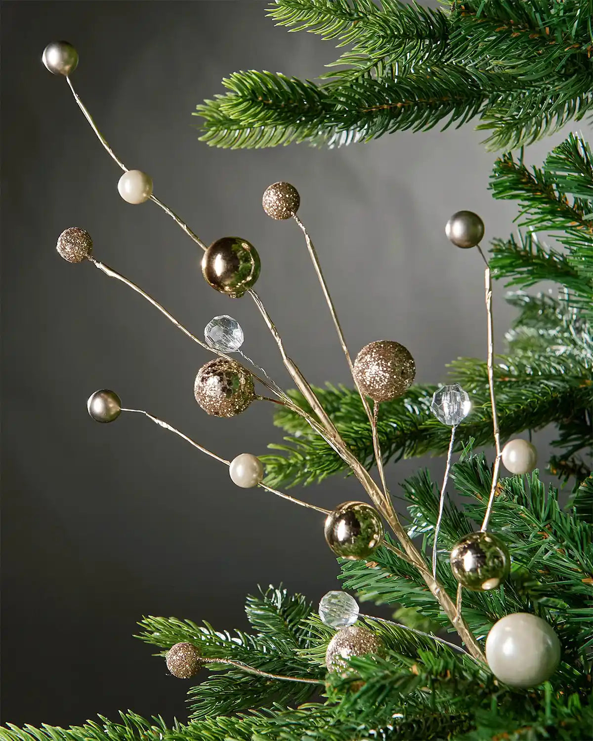 Full image of gold bauble and jewelled spray attached to tree in front of grey wall background