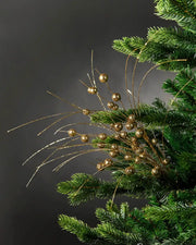 Full image of gold glitter berry spray attached to Christmas tree in front of grey wall background