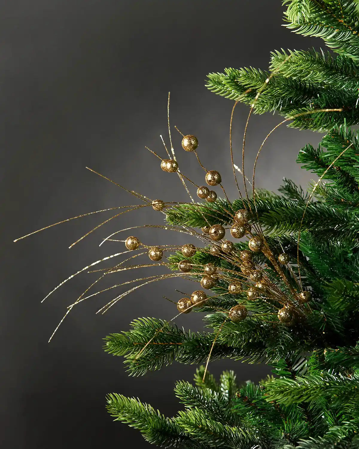 Full image of gold glitter berry spray attached to Christmas tree in front of grey wall background