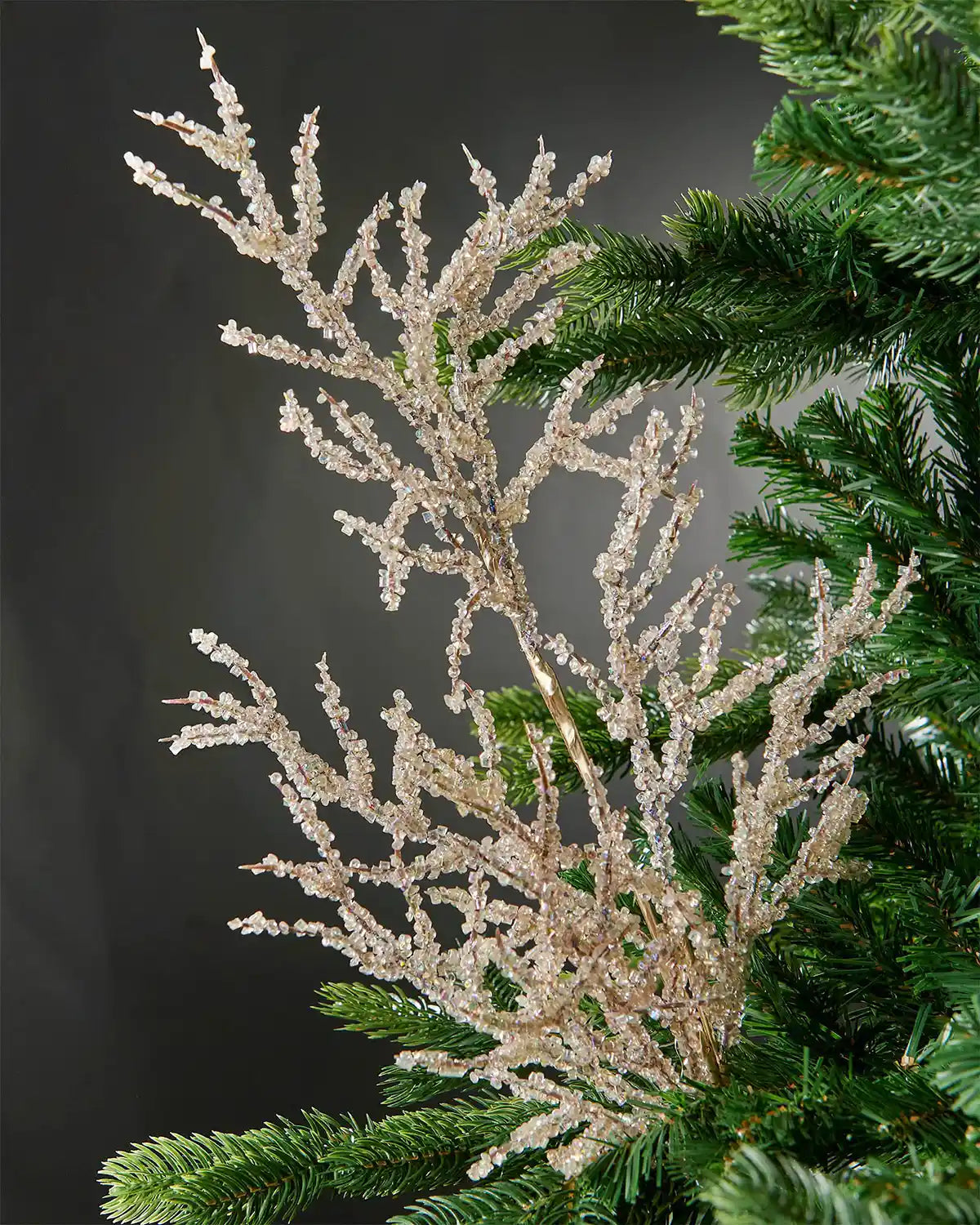 Full image of gold beaded crystal spray attached to Christmas tree in front of grey wall background