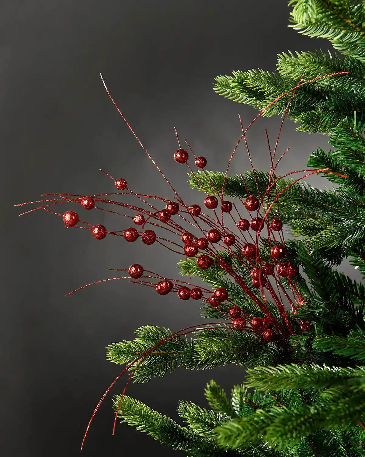 Full image of red glitter berry spray decor attached to Christmas tree in front of grey wall background