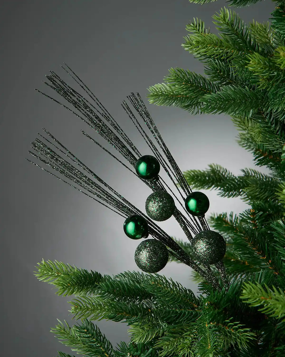 Full image of sage green glitter bauble spray inside Christmas tree in front of grey background