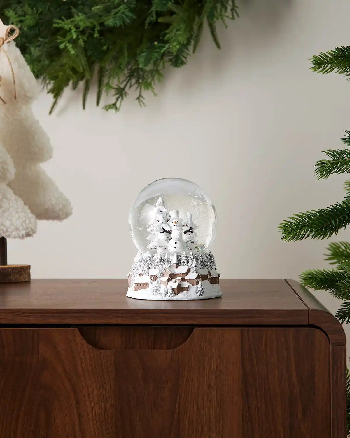 Full image of snowman snow globe resting on dark wood surface in front of white wall background
