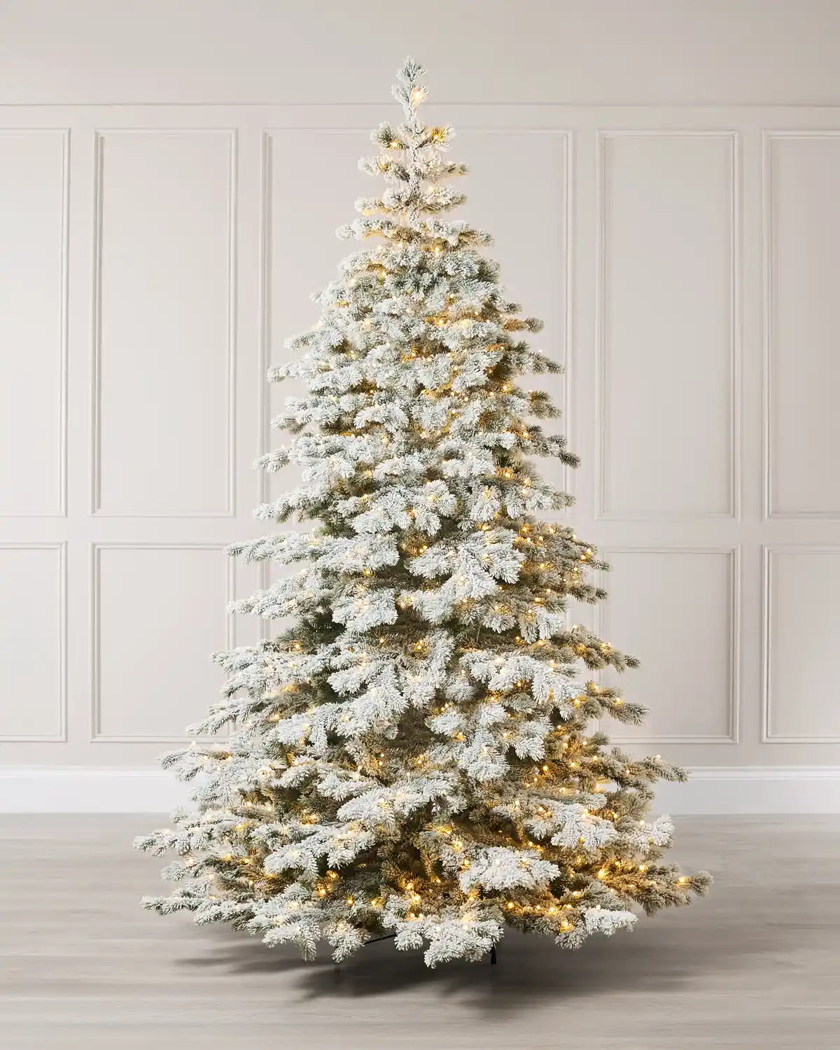 Full view of a snow-flocked artificial Christmas tree with warm white LED lights